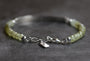 A beaded bracelet with pale yellow-green faceted beads and silver-tone chain detailing, clasp, and small hanging tag, photographed on a dark gray textured surface.