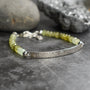 A beaded bracelet with pale yellow-green translucent beads and an engraved silver bar, photographed on a dark textured surface with blurred stones in the background.