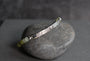 A sterling silver celtic engraved bar bracelet with 5mm faceted pale green to dark green gemstone beads, displayed on a smooth dark gray stone against a dark gray background.