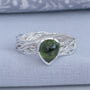 A sterling silver ring with a twisted, braided band and a teardrop-shaped green gemstone, displayed on a textured light blue fabric surface.