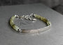 A gemstone neaded bar bracelet featuring a textured sterling silver ID style Celtic bar and a beaded strand of pale yellow-green gemstone beads, resting on a gray textured surface.